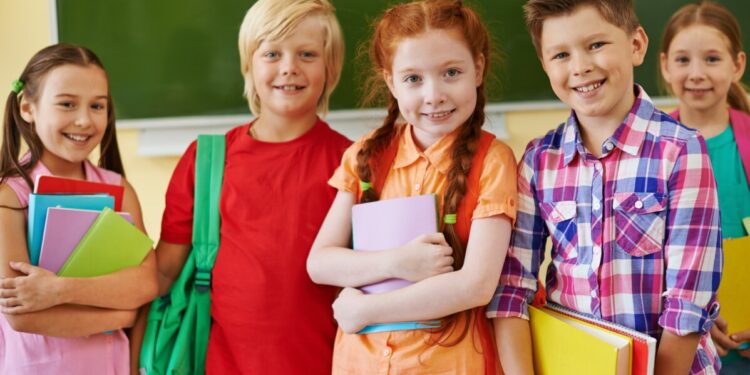 Five friendly classmates looking at camera on background of blackboard