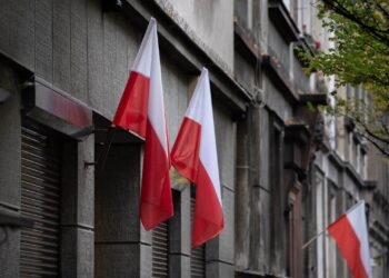 Flagi Polski wywieszone na elewacji kamienicy przy miejskiej ulicy