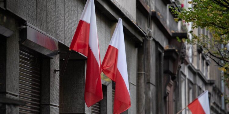 Flagi Polski wywieszone na elewacji kamienicy przy miejskiej ulicy