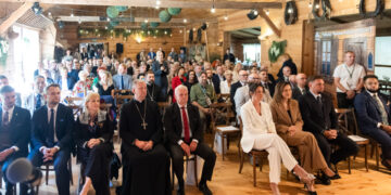 Goście jubileuszu dziesięciolecia Podlaskiego Muzeum Kultury Ludowej w drewnianej sali, w tle szyld muzeum