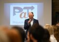 Uczestnik spotkania inaugurującego program PaT przemawia przy ekranie z logo