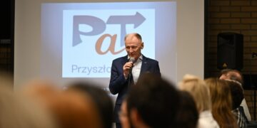 Uczestnik spotkania inaugurującego program PaT przemawia przy ekranie z logo