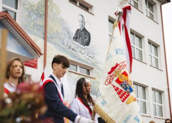 Poczet sztandarowy przed budynkiem szkoły podstawowej w Korycinie z muralem patrona