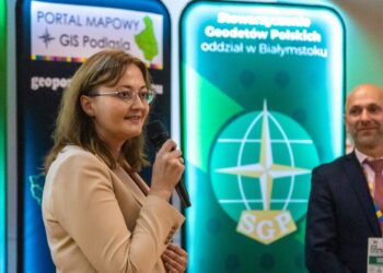 Uczestnik Podlaskiego Forum GIS przemawia przy ekranie z logo portalu mapowego