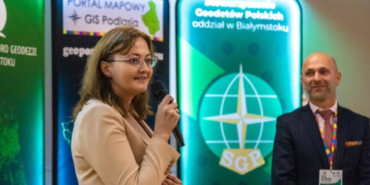 Uczestnik Podlaskiego Forum GIS przemawia przy ekranie z logo portalu mapowego