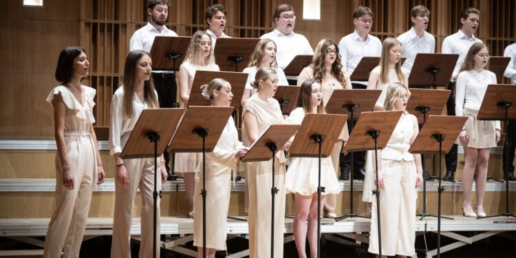 Chór Młodzieżowy Opery i Filharmonii Podlaskiej podczas koncertu, śpiewacy w jasnych strojach przy pulpitach z nutami