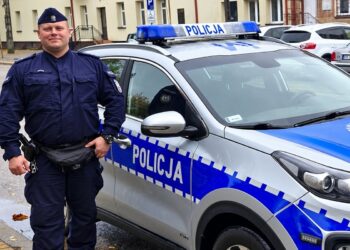 Policjant stojący przy radiowozie na ulicy w Szczuczynie