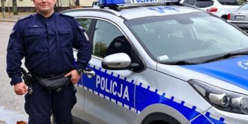 Policjant stojący przy radiowozie na ulicy w Szczuczynie