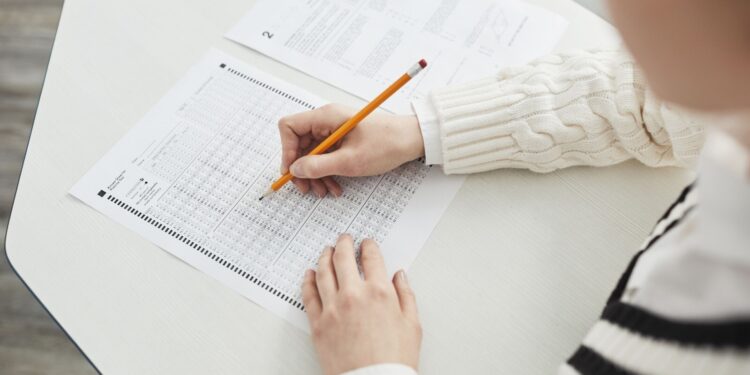 Uczeń wypełnia ołówkiem kartę odpowiedzi testu na szkolnej ławce