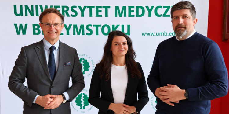 Troje naukowców Uniwersytetu Medycznego w Białymstoku przed banerem uczelni