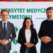 Troje naukowców Uniwersytetu Medycznego w Białymstoku przed banerem uczelni
