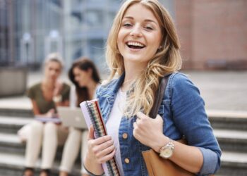 Studentka z notatnikami przed budynkiem uczelni