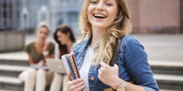 Studentka z notatnikami przed budynkiem uczelni