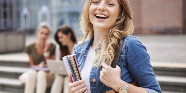 Studentka z notatnikami przed budynkiem uczelni