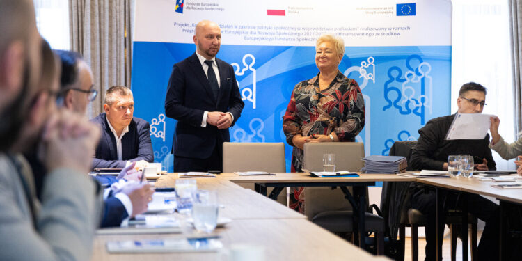 Uczestnicy posiedzenia komitetu przy stole konferencyjnym, w tle baner projektu