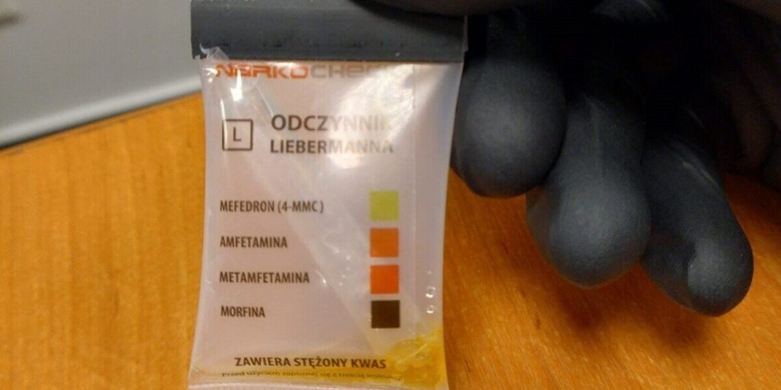 Policyjny narkotest w dłoni funkcjonariusza z zaznaczonym wynikiem wskazującym mefedron